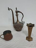Photo showing the full lot including antique Qajar Persian copper ewer, ornate metal cup, and Art Deco metal vase on white surface.
