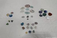 Top-down view showing several collections of polished stones arranged in groups, including engraved stones with words, plain polished stones, heart-shaped stones, and glass beads with dried flowers.