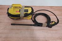 Yellow Karcher 410 electric pressure washer unit with electrical cord wrapped around it and black hose with attached spray gun laid out on wooden surface.