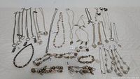 Full view of over 30 silver-toned metal jewelry pieces arranged on a quilted surface showing necklaces, bracelets, and earrings with tags.