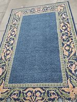 Full view of vintage deco style rug showing blue ripple patterned center and floral scrolling border, size approximately 5 feet by 8 feet.