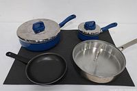 Top view photo of all four cookware pieces showing lids and handles on two blue T-Fal pots, one stainless Calphalon pan and one black Chefmate fry pan.