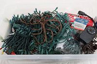 Plastic tub filled with tangled green and brown corded Christmas light strands, plus other items.
