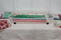 Plastic wheeled storage tub filled with several rolls of Christmas-themed wrapping paper and some gift bags outside the tub