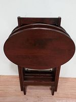 Front view of the oval mahogany wood TV tray stands stacked together showing dark brown finish and smooth tabletop surface.