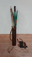 Full view of the vintage bow and arrow set including brown leather case filled with arrows, unstrung bow and gloves laid out