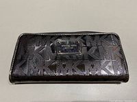 Michael Kors wallet showing black textured monogram and brand plaque