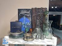 Overview of entire barware lot showing crystal decanter with stopper, wooden wine case, bottle coaster box, vintage metal shot glasses, and glass carafes.