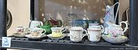 Full shelf view showing bone china teapot, assorted teacups, saucers, other pottery teapots and pitcher