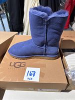 Image of a single blue Ugg Bailey Button boot on top of a Ugg Australia branded box with a handwritten lot number sticker.