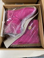 Pair of bright pink UGG boots still in clear plastic bags inside original box.