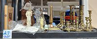 Overview showing multiple brass candle holders, religious figurines, rosaries, and other items on shelf