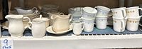 Display of Corelle cups, creamers, pitchers and plates on shelf showing various patterns including Country Violet and floral designs.