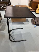 Black adjustable side table with tray top and foldable tubular metal legs shown upright