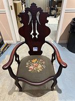 Front view of vintage wooden armchair showing carved back featuring two stylized lion heads with wings and curved armrests.
