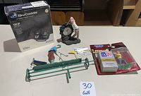 Wide view of entire golf memorabilia lot showing boxed SkyCaddie SG5 set, golf figures, tees, divot tools, and desk clock on a table.