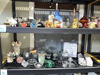 Clear view of black shelving with various glass votive holders, angel statues, glass sconce globes, and candles on two shelves