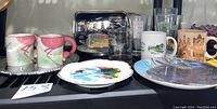 Side view focusing on souvenir mugs and plates displayed together on shelf