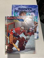 Two Sports Illustrated magazines stacked, one with an ice hockey goal tender on the cover and another with a 2023 MLB preview baseball cover.