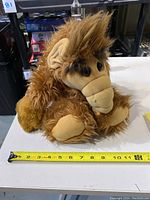 Brown vintage Alf plush toy on white table with measuring tape showing approx 11 inches length