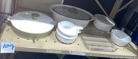 Display of vintage CorningWare set showing large covered casserole, covered roaster, plastic-covered baking dish, Grab-It bowls, small saucepan, and rectangular Pyrex dish.