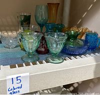 Various colored vintage glassware including amber, blue, green, and cranberry pieces on a shelf.