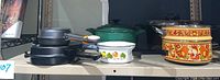 Side view of most ceramic and cast iron pans including green Dutch oven, yellow double boiler, fry pans and omelette pans.