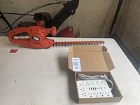 Full view of Black & Decker electric hedge trimmer and multi-port power strip in box on a white table.
