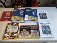 Top view of a collection of coin, stamp, and postcard collecting reference books spread on a white table.