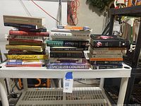 Wide view of stack of varied books on a white table revealing title details and overall condition.