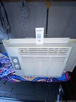 Front view of GE window air conditioner showing manual rotary dial controls, horizontal and vertical vents, and attached mounting brackets.