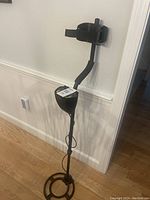 Full length view of black metal detector showing padded armrest, curved shaft, and circular search coil.