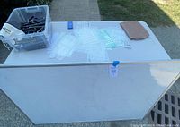 Large whiteboard, plastic bin with markers and pens, various stencils, and notebook cover on table outdoors.