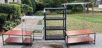 Overview of two plastic shelving units (white and black), two wooden-top benches/low shelves with black metal frames, and a metal rolling clothes rack outdoors.