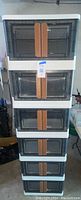 Front view of six stacked plastic storage units with tinted transparent latching doors and brown handles.