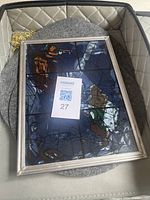 Stained glass panel in metal frame lying on quilted carrier with golden chain visible.