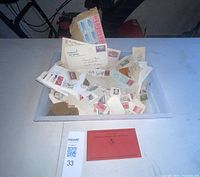 Top-down view of a plastic bin filled with numerous vintage and antique stamps primarily on envelopes and postcards, along with some loose stamps.