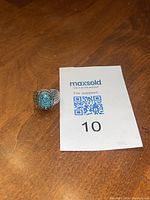 Silver ring with oval turquoise stone on wooden surface alongside a lot card showing number 10.