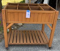Front view of a wooden raised garden planter with labeled tag attached, showing six compartments and bottom slatted shelf.