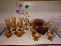 Full view of all 31 amber glassware pieces including plates stacked, wine glasses, small bowls, and creamer and sugar bowl in front.