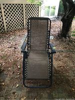 Front view of folding anti gravity lounge chair showing metal frame, mesh seat, and attached armrests, positioned outdoors on ground with dry leaves.