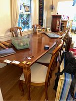 Set of six wooden dining chairs positioned around a wooden dining table in a room with hardwood floors and stained glass window.