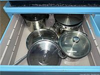 Drawer containing stainless steel pots with lids and perforated pots for straining or steaming