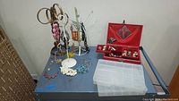 Photo of assorted costume jewelry displayed on metal jewelry trees and flat surface including bracelets, necklaces, and earrings.