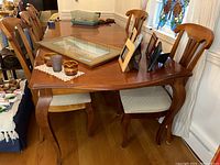 Photo showing wooden dining table with four matching chairs, table surface with items not included in sale