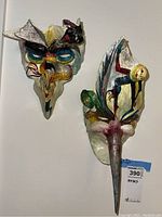 Set of two colorful, abstract folk art papier-mâché masks on a flat surface.