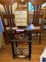 Jewelry box displayed on small wooden stand with several decorative wooden trays underneath and nearby.