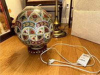 Full view of the lamp showing the spherical globe with floral patterns and attached power cord on wooden base.