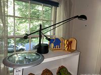 Desk lamp with long adjustable arm, wooden bookends featuring blue elephant and red monkey, all placed on a white cabinet near window.