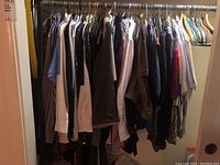Wide view of men's clothes hanging including shirts, pants, sweaters, ties, and belts with hangers